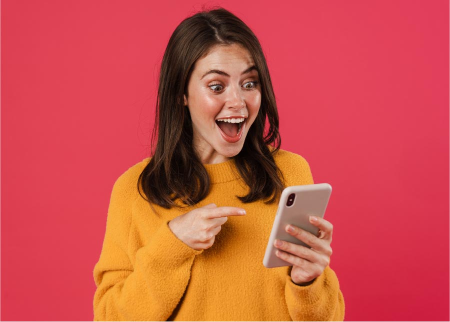 Femme joyeuse tenant un smartphone, illustrant l’inscription simple et rapide à l’examen du code de la route en ligne ou sans rendez-vous